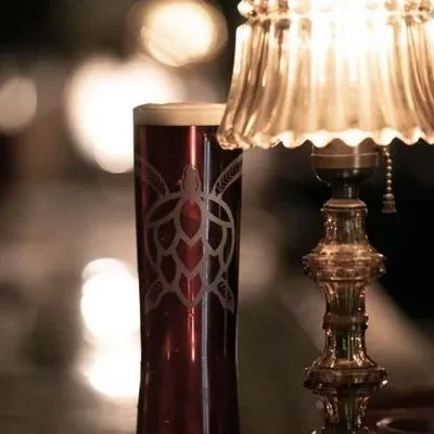 Dark beer in a tall glass with etched hop-turtle, warm lamp glow.