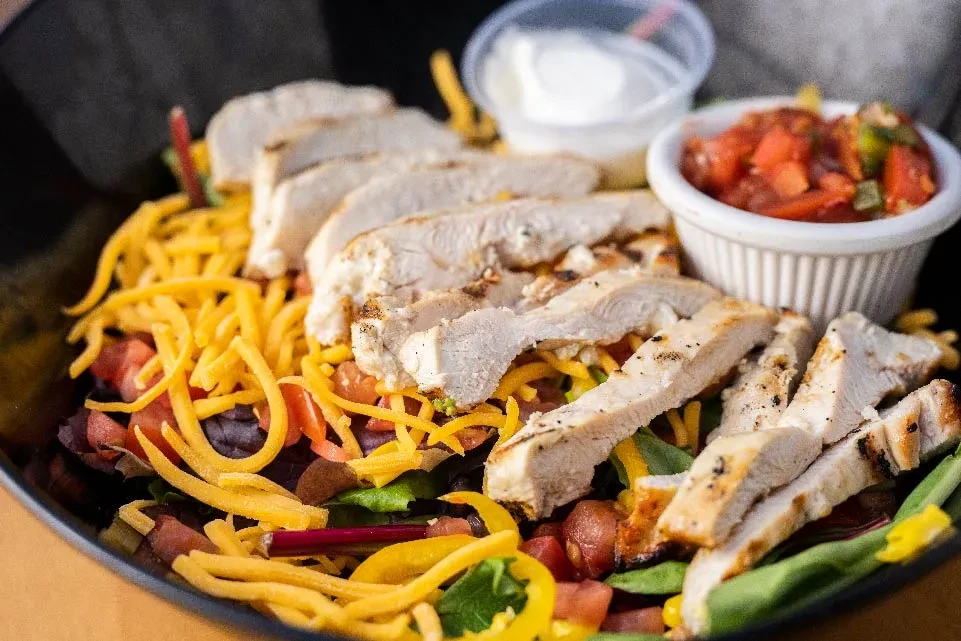 Grilled chicken salad, cheese, tomatoes, bell peppers, with side sauces.