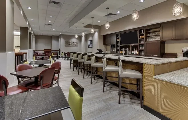 Modern restaurant interior with colorful seating, a granite bar, and liquor display.