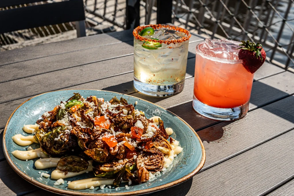 Roasted Brussels sprouts, two cocktails on a sunlit outdoor table.