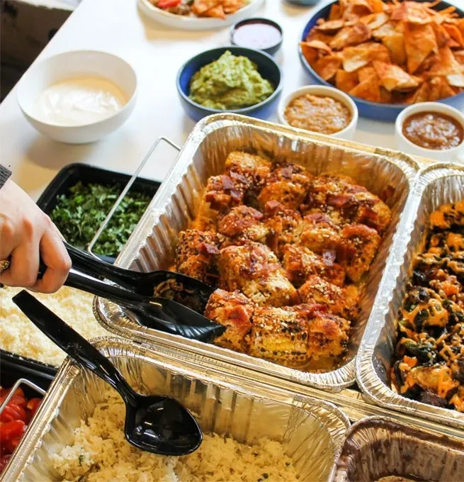 Buffet line with hand serving sauced chicken, rice, and condiments.