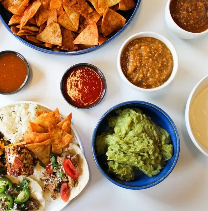 Overhead display of Mexican tacos, chips, guacamole, and various salsas.