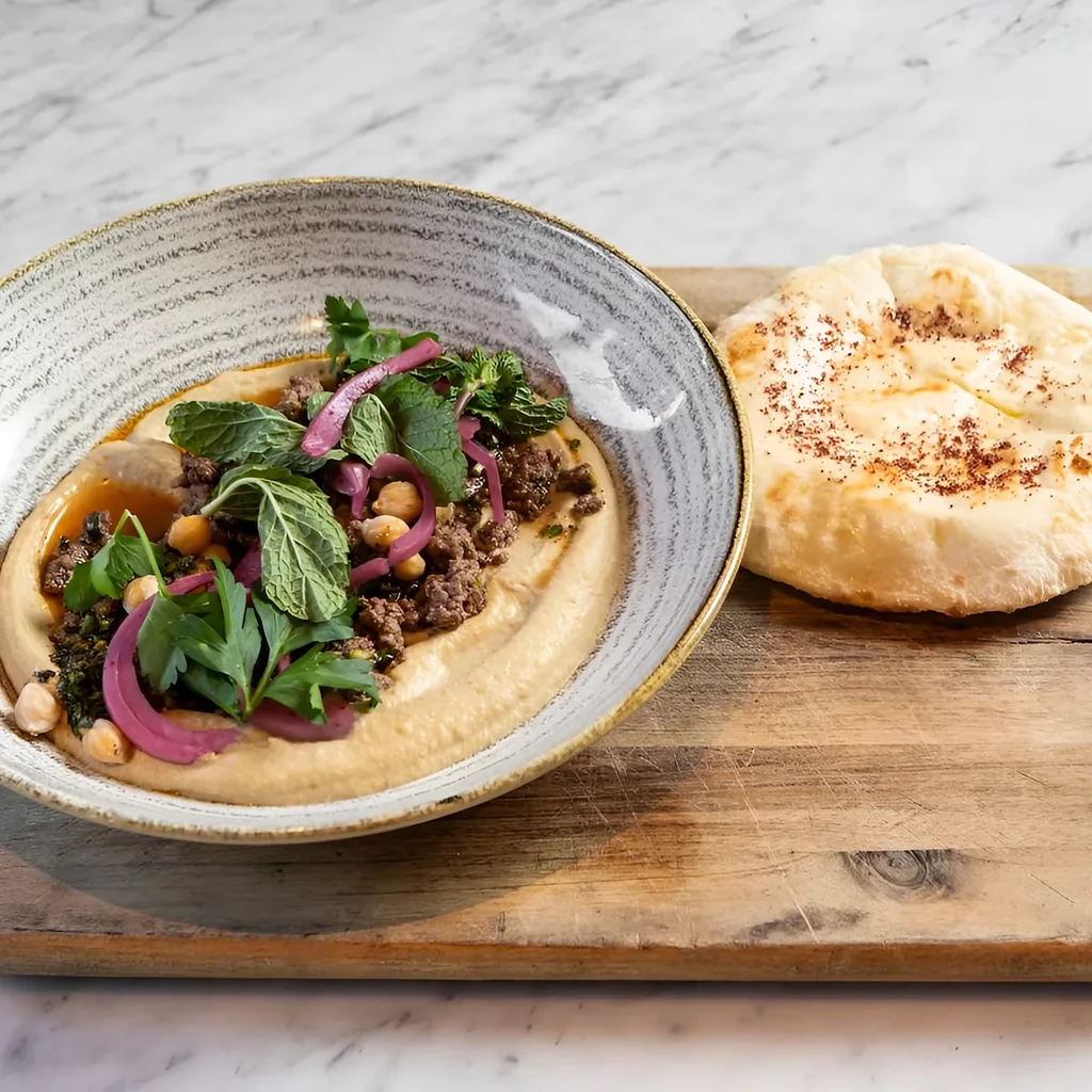 Hummus bowl topped with ground meat, chickpeas, herbs, onions, and pita.