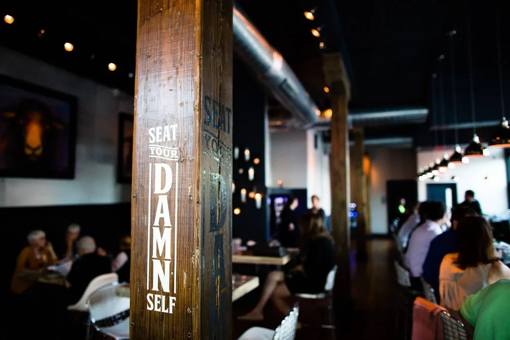 Weathered wooden pillar reads 'SEAT YOUR DAMN SELF' in a restaurant.