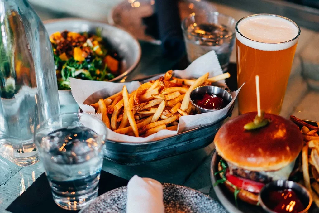 Wooden table laden with fries, ketchup, burger, beer, and salad.
