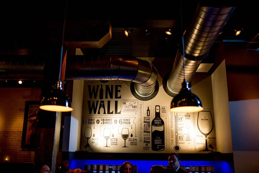Modern wine bar with exposed ductwork and informational 'WINE WALL' mural.