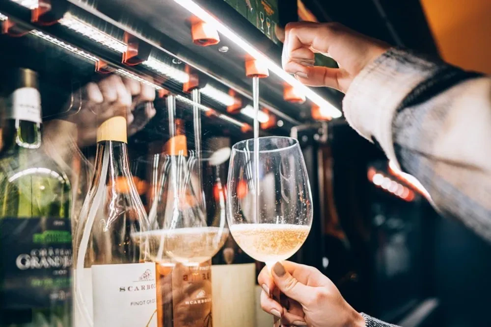 Close-up: Hand holds glass under dispenser pouring sparkling wine.