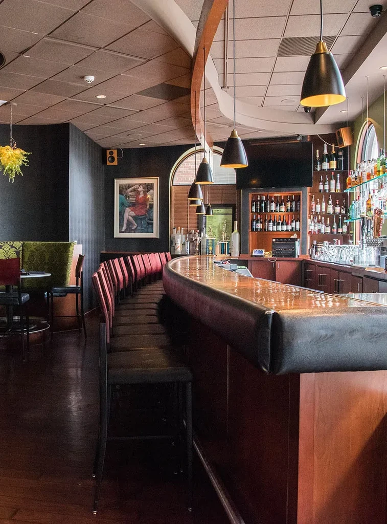 Empty upscale bar with curved counter, red stools, and liquor bottles.