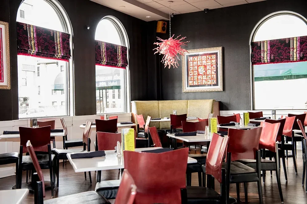 Empty modern restaurant dining room, dark walls, white tables, red chandelier.