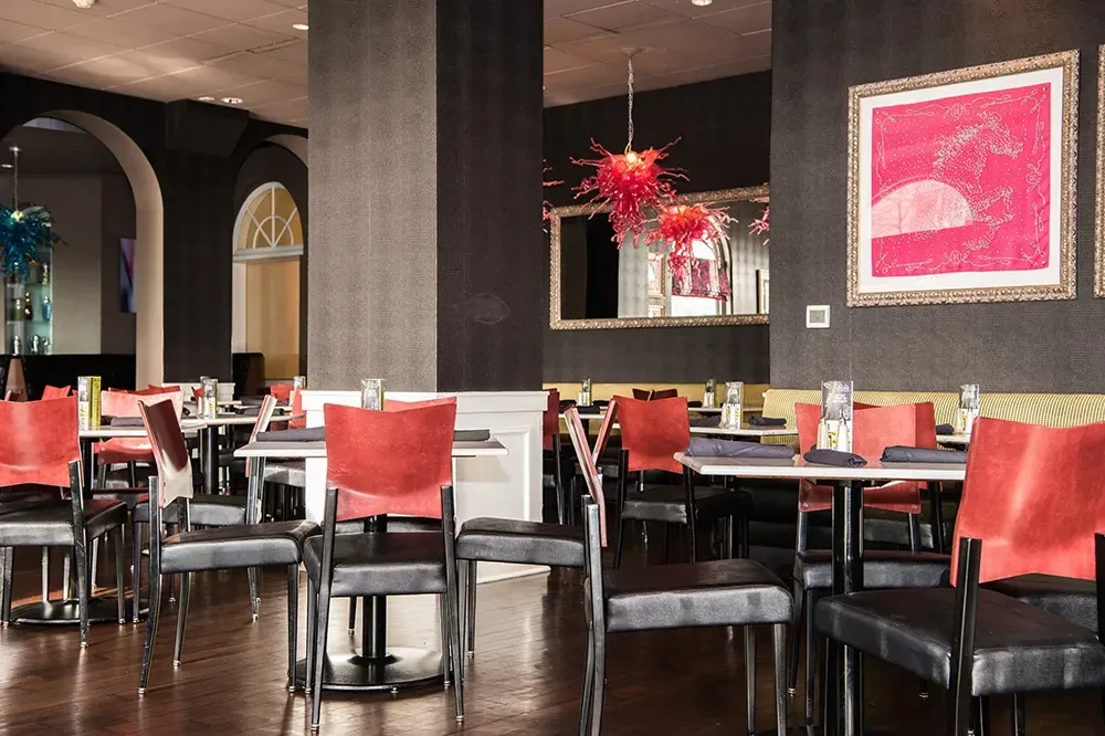 Modern restaurant interior with red chairs, spiky chandeliers, and horse artwork.