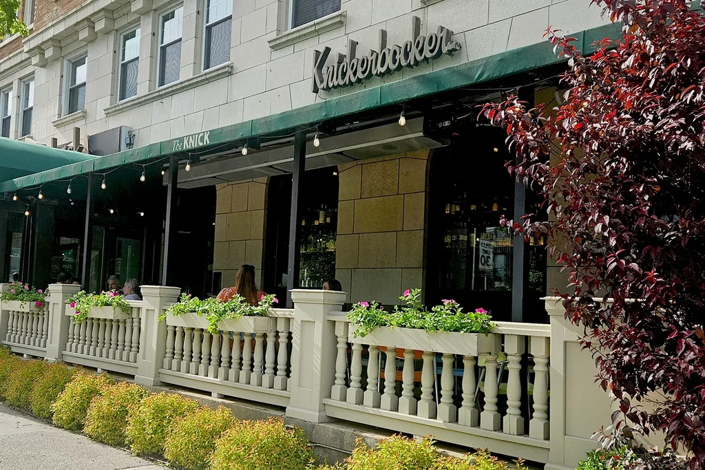 Exterior of The Knick patio with green awning, flowers, and people.