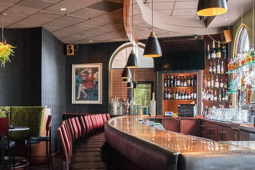 Stylish bar interior with a curved counter, bottle display, and booth seating.