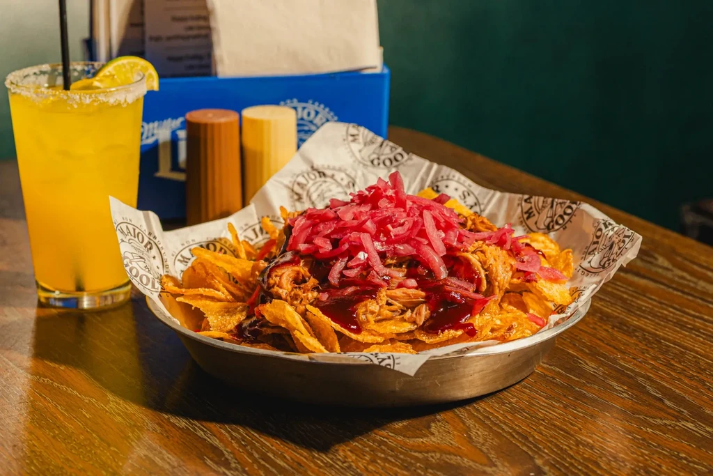 Loaded fries with BBQ sauce, pickled onions, and a yellow cocktail.