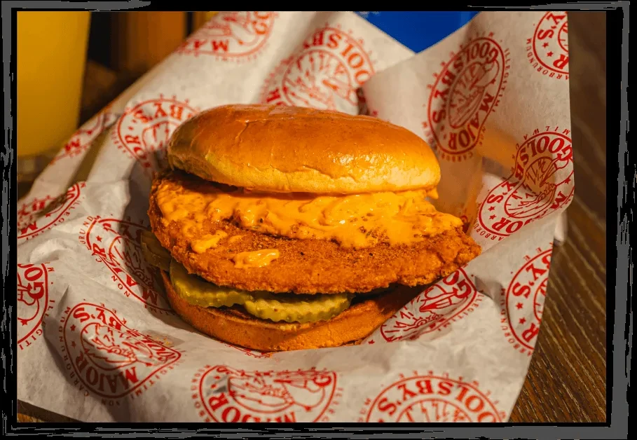 Chicken sandwich with melted orange cheese and pickles on branded paper.
