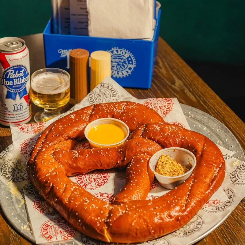 Large salted pretzel with cheese, mustard, beer, and restaurant branding.