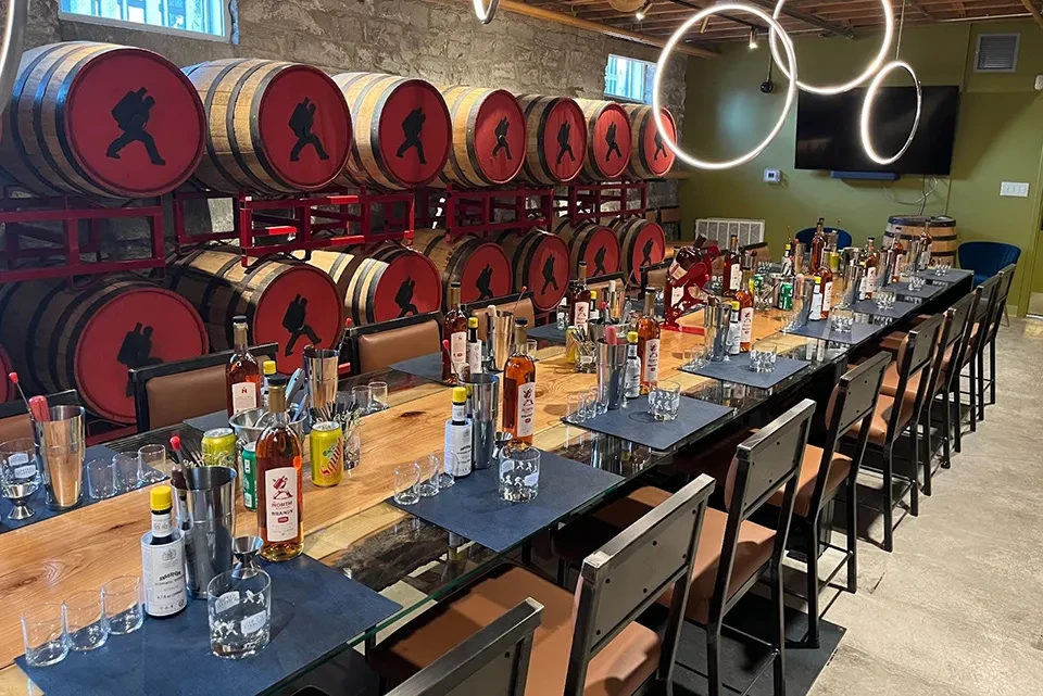 Rustic tasting table with spirits, glassware, bar stools, and barrel display.