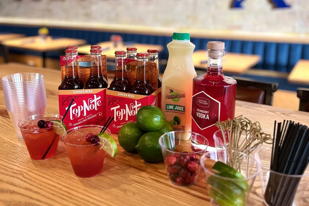 Cocktail ingredients, drinks, and garnishes on a wooden table.