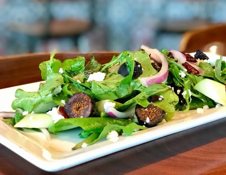 Fresh arugula salad with figs, crumbled cheese, red onion, and dried fruit.