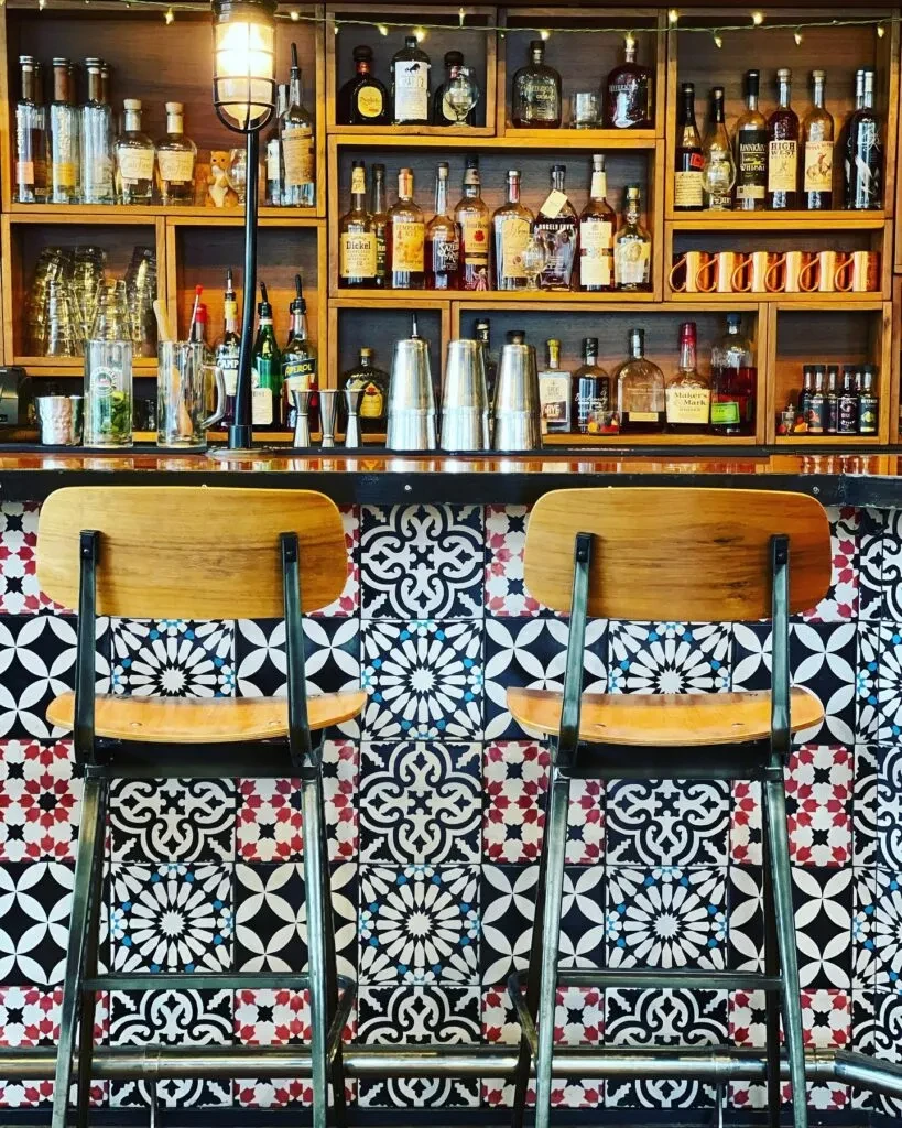 Bar counter with liquor bottles, mosaic tile facade, and barstools.
