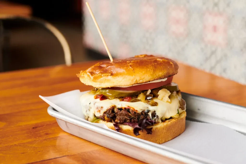 Close-up burger with beef, melted cheese, tomato, and jalapeños on a tray.
