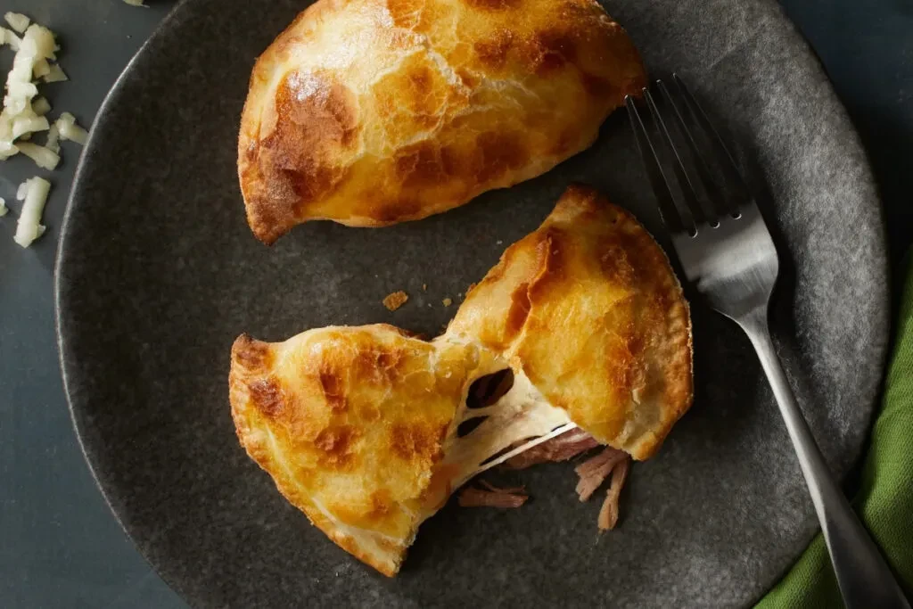 Two golden pastries, one cut to show meat and melted cheese.