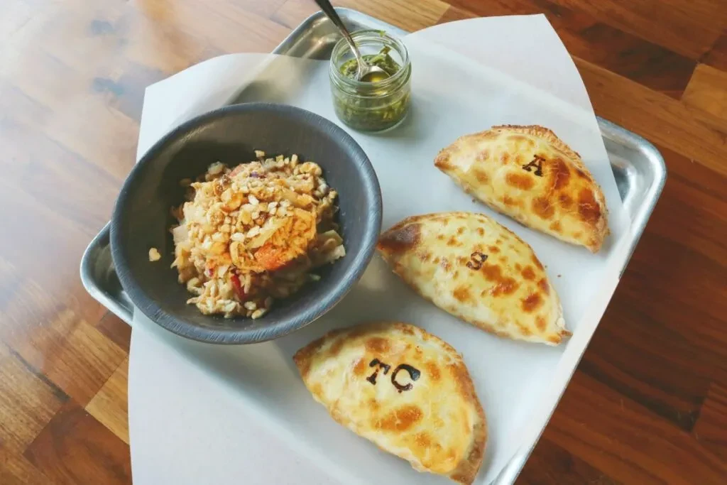 Silver tray with grain bowl, green sauce, and three branded empanadas.