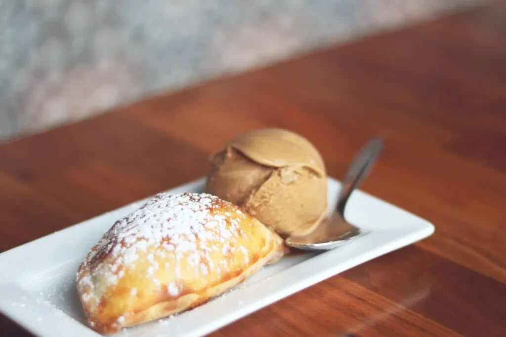 Sugar-dusted pastry, ice cream, and spoon on a white plate.