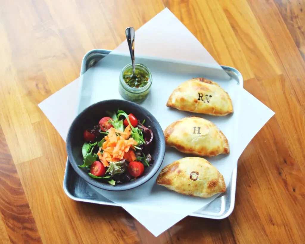 Three lettered empanadas, side salad, and green sauce on a tray.