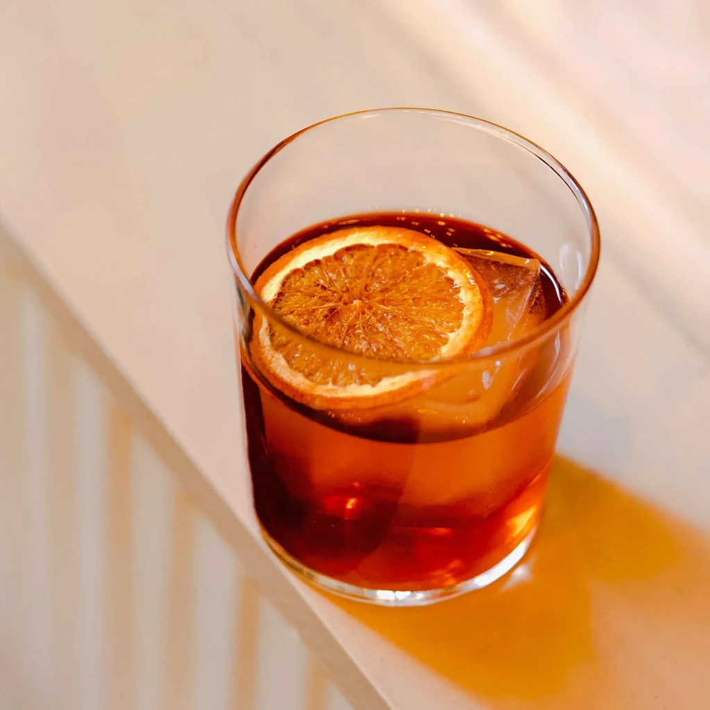 A single amber cocktail with ice and a dried orange garnish.
