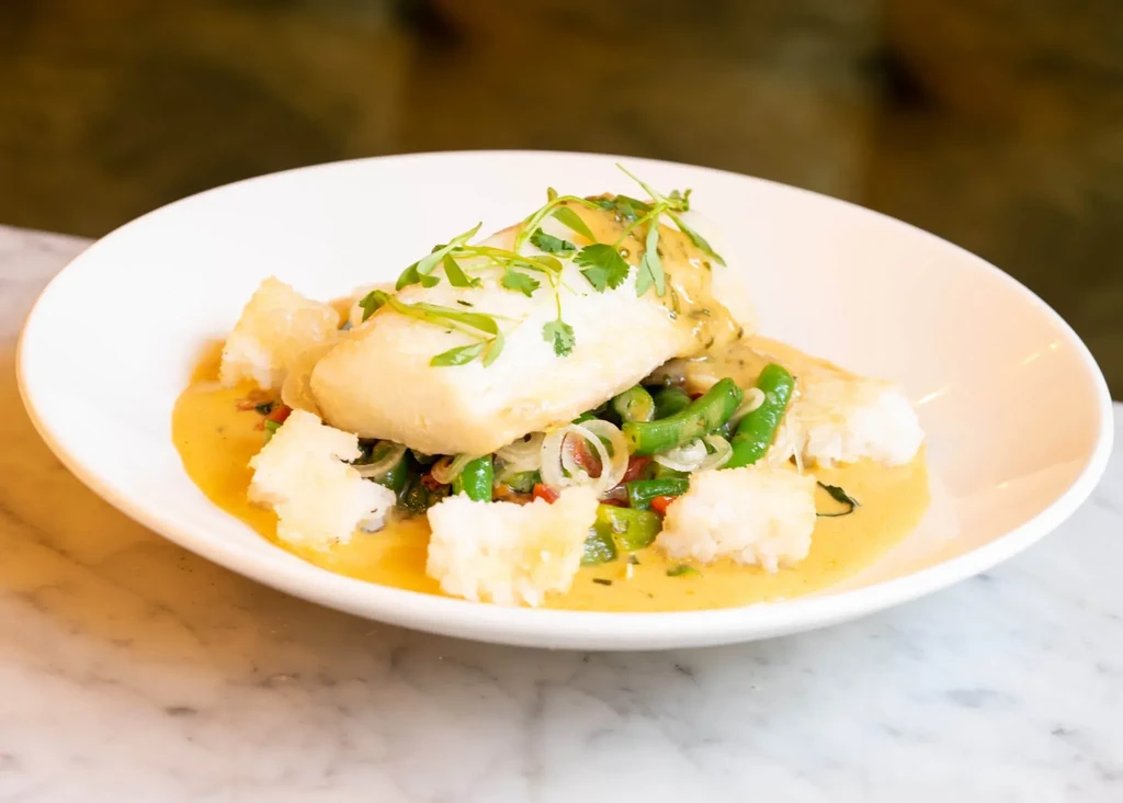 White fish with herbed sauce, colorful vegetables, and crispy sides.