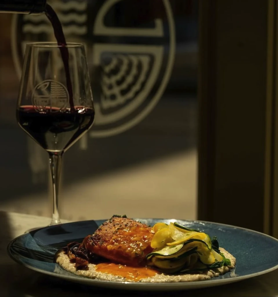Close-up of plated protein and vegetables with red wine pouring.