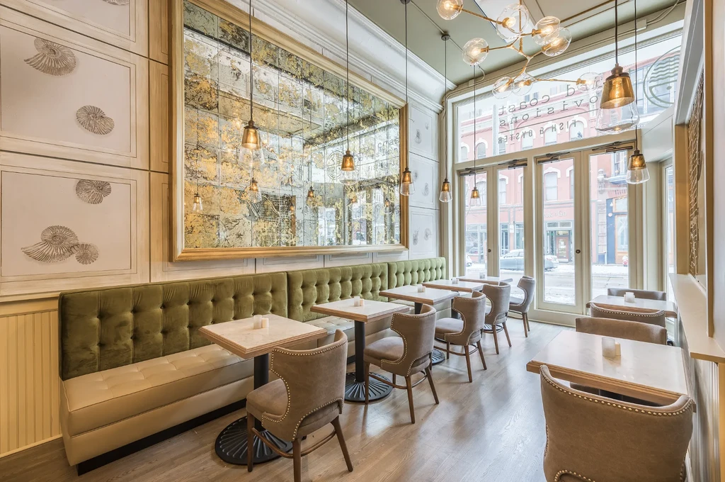 Elegant restaurant dining room with green banquette, marble tables, and gold mirror.