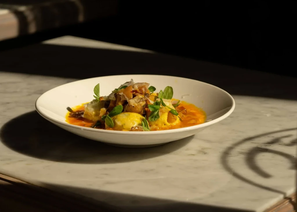 Gourmet pasta or dumplings with orange sauce, mushrooms, parmesan, microgreens.