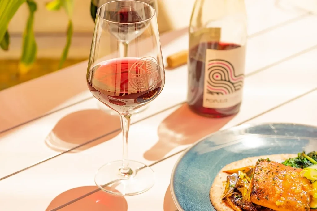 Etched wine glass, red wine bottle, and fish dish on a dining table.