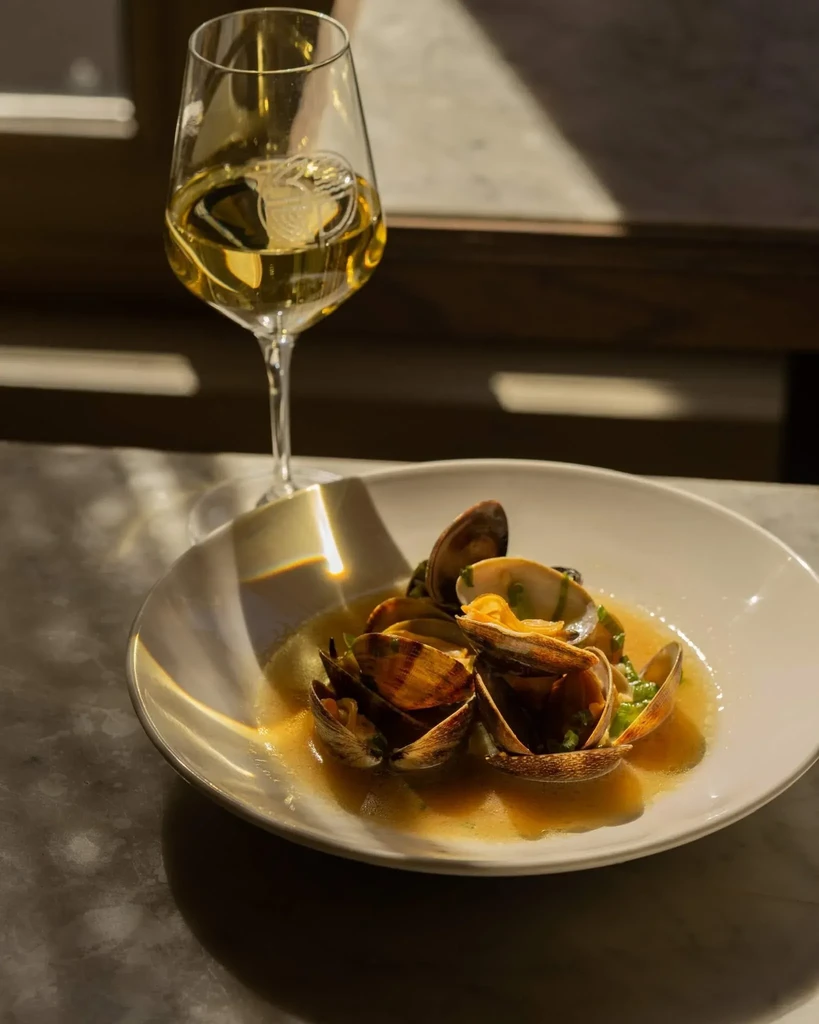 Close-up of steamed clams with herbs and white wine on a table.