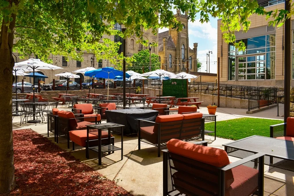 Sunny outdoor patio with varied seating, umbrellas, and urban buildings.