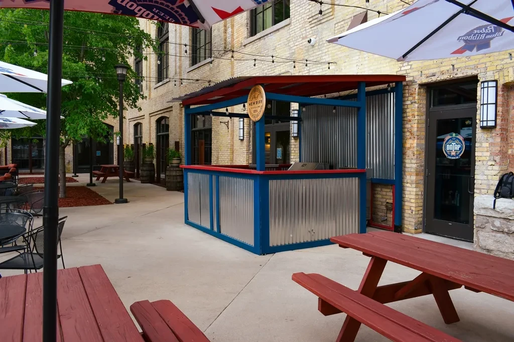 Empty outdoor patio with tables, New Riff Distilling bar, and string lights.