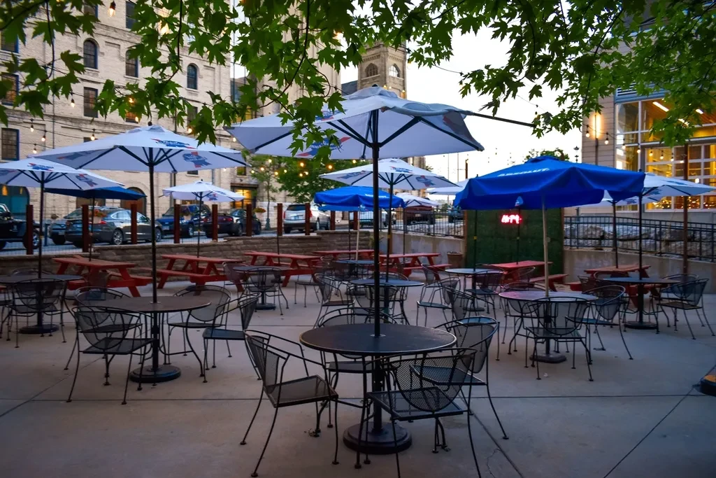 Outdoor restaurant patio with tables, branded umbrellas, and pink neon sign.