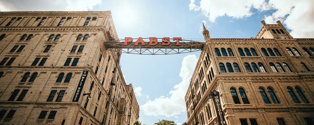Historic brick buildings connected by 'PABST' skywalk, 'MALT HOUSE' sign visible.