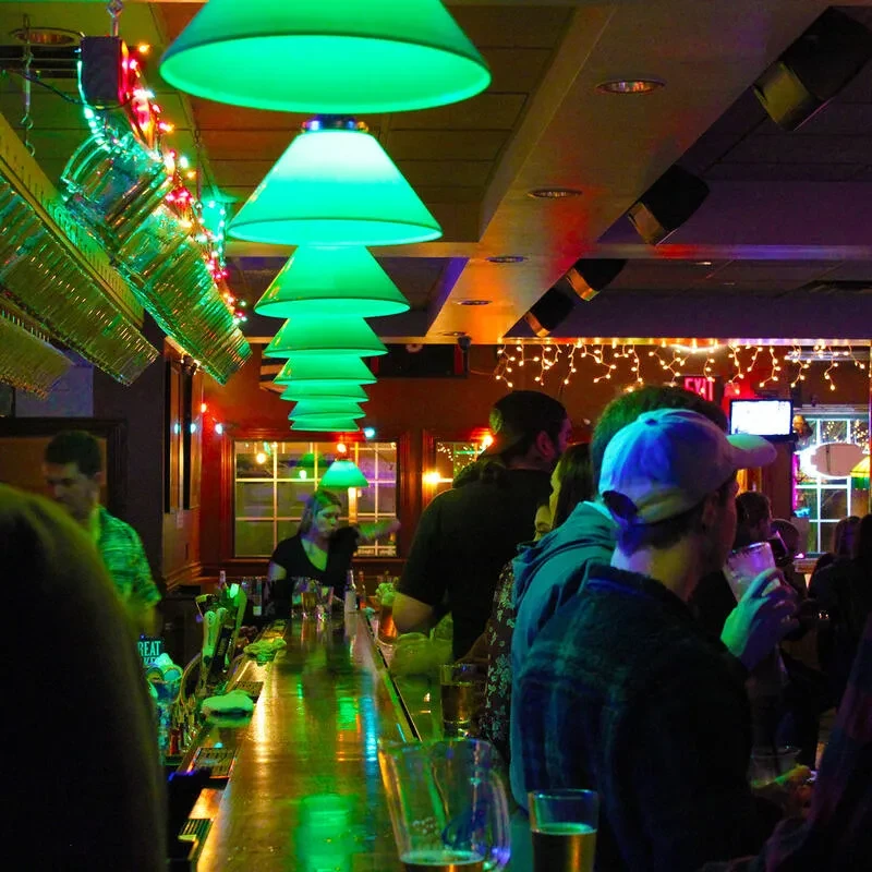 Lively bar with green pendant lights, colorful string lights, and patrons.