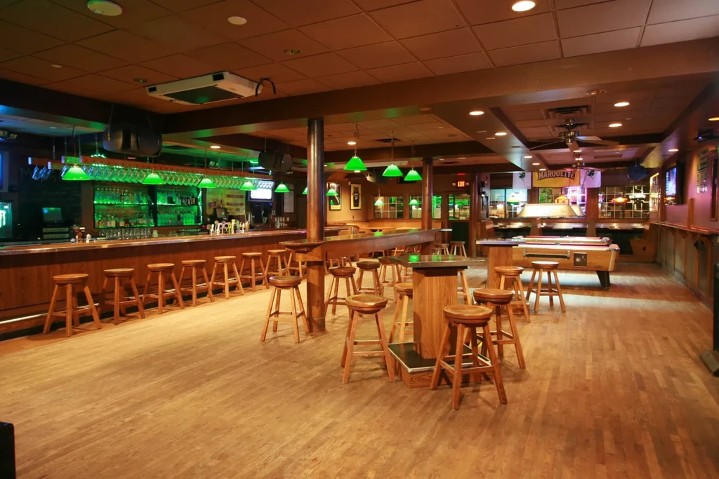 Empty Marquette bar interior with green-lit wooden bar and pool table.