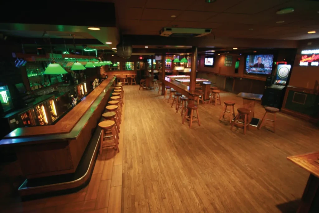 Dimly lit, empty sports bar with wooden bar, tables, and TVs.