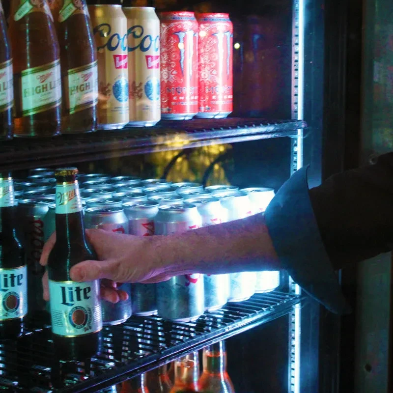 Arm retrieves Miller Lite from a blue-lit beverage display.