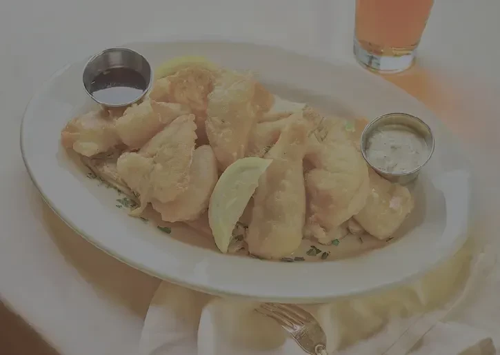 Platter of golden fried food with lemon and two sauces.