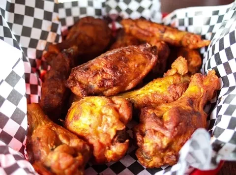 Close-up of golden-brown fried chicken pieces in a checkered basket.