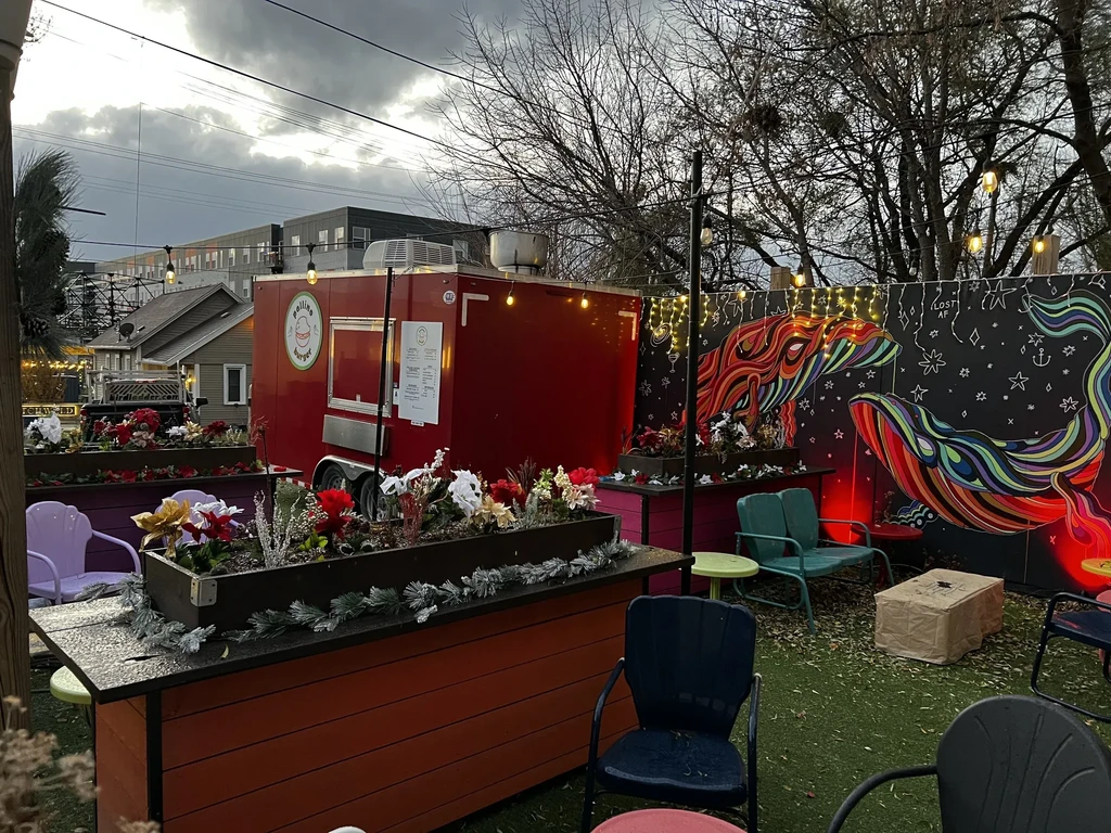 Vibrant outdoor patio, red food truck, winter planters, and colorful whale mural.