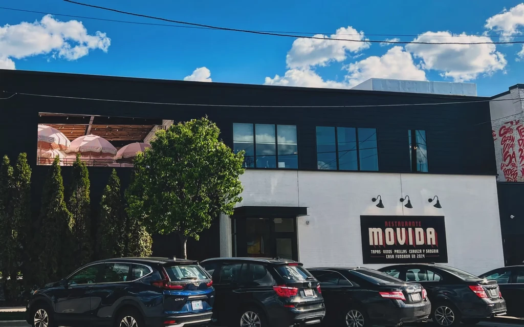 Movida restaurant exterior: modern building, patio, parked cars, red graffiti.