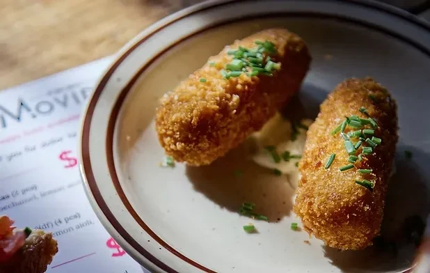 Two golden-brown croquettes with chives and white sauce on a plate.