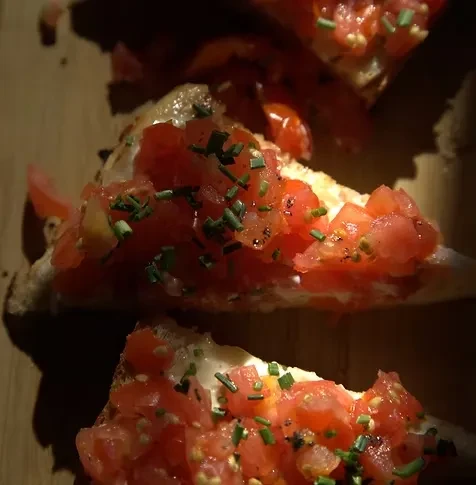 Two triangular bruschetta with diced tomatoes, chives, and creamy spread.