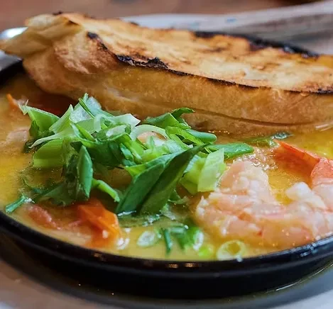 Close-up of creamy shrimp broth with green onions and grilled bread.